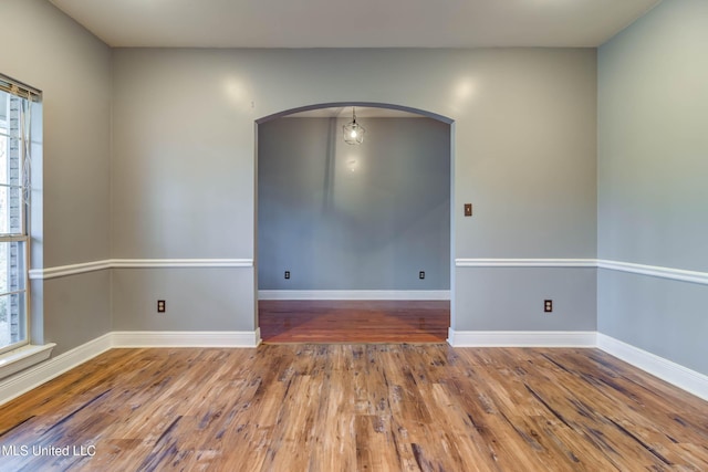 spare room featuring baseboards, arched walkways, and hardwood / wood-style floors