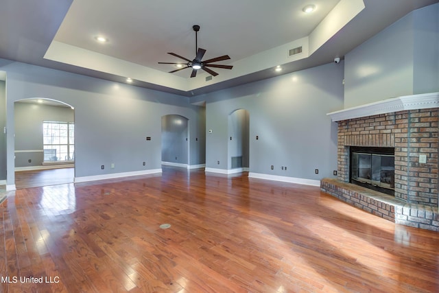 unfurnished living room with a ceiling fan, arched walkways, a brick fireplace, and visible vents