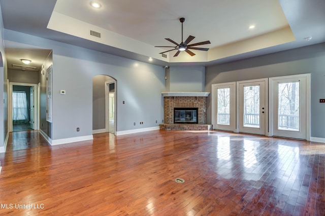 unfurnished living room featuring a tray ceiling, wood-type flooring, a fireplace, and baseboards