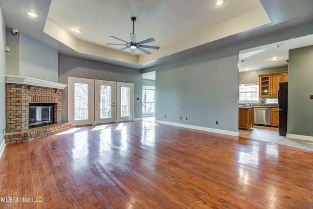 unfurnished living room with light wood-style flooring, a fireplace, a tray ceiling, and baseboards