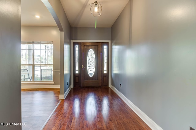 foyer featuring baseboards, arched walkways, and wood finished floors