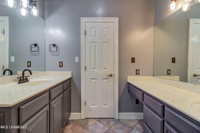 bathroom featuring two vanities, a sink, and baseboards