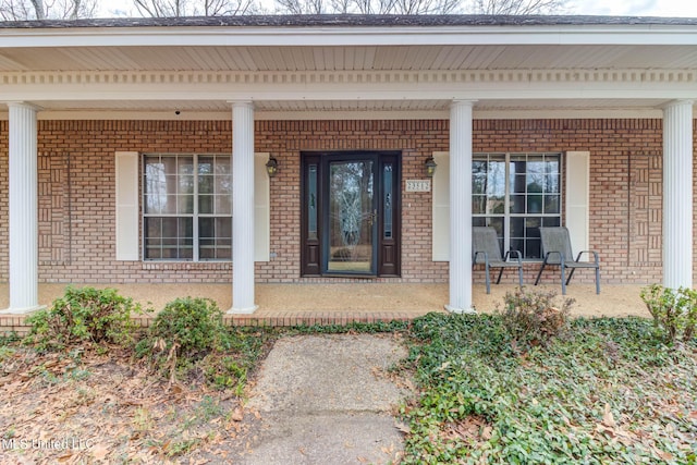 view of exterior entry with a porch and brick siding