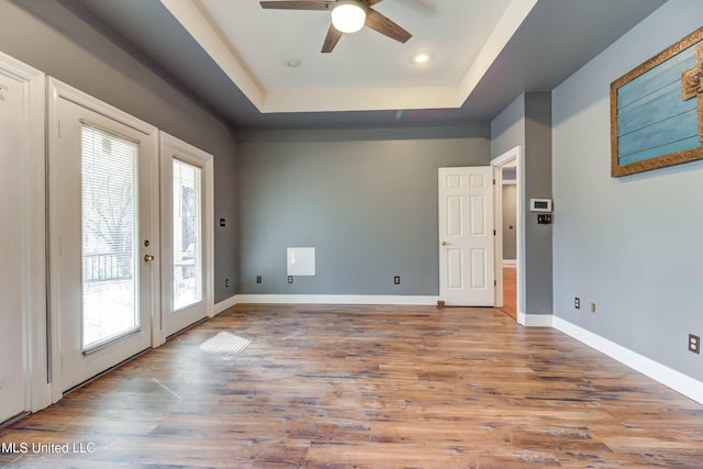 spare room with a tray ceiling, french doors, ceiling fan, wood finished floors, and baseboards