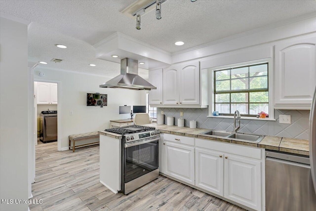 110 Stonington Ct, Brandon, MS 39047 - kitchen featuring wall chimney range hood, appliances with stainless steel finishes, washer / clothes dryer, tile counters, and white cabinetry