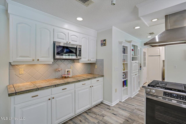 110 Stonington Ct, Brandon, MS 39047 - kitchen with stainless steel appliances, wall chimney range hood, light wood-style floors, white cabinetry, and decorative backsplash