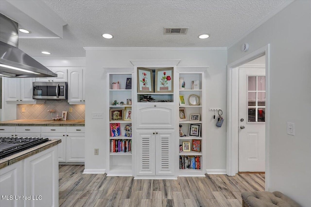 110 Stonington Ct, Brandon, MS 39047 - kitchen featuring stainless steel microwave, wall chimney exhaust hood, light wood-type flooring, white cabinetry, and tasteful backsplash