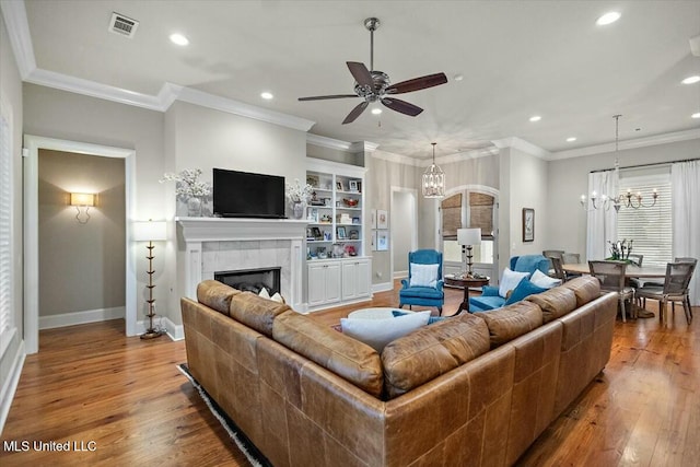 living room featuring crown molding, a fireplace, ceiling fan with notable chandelier, and hardwood / wood-style flooring