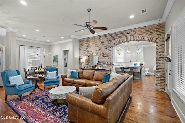 living room with hardwood / wood-style floors, ceiling fan with notable chandelier, sink, crown molding, and brick wall