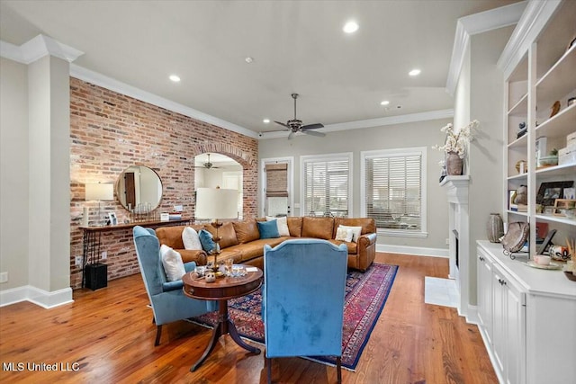 living room with light hardwood / wood-style floors, ceiling fan, crown molding, and brick wall