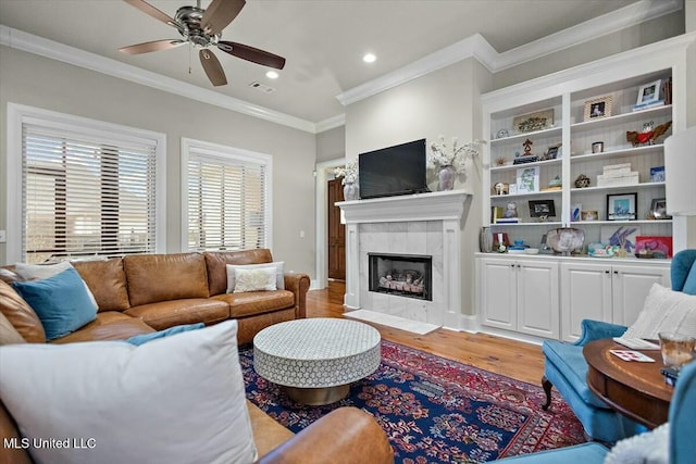 living room featuring hardwood / wood-style flooring, ceiling fan, crown molding, and a tiled fireplace