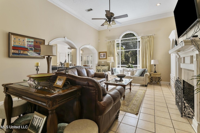 living area featuring light tile patterned floors, arched walkways, a ceiling fan, ornamental molding, and a fireplace