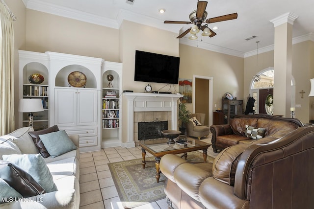 living area with light tile patterned floors, decorative columns, a tiled fireplace, ceiling fan, and crown molding