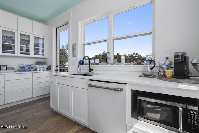 kitchen featuring stainless steel microwave, a sink, glass insert cabinets, white cabinets, and dark wood-style flooring