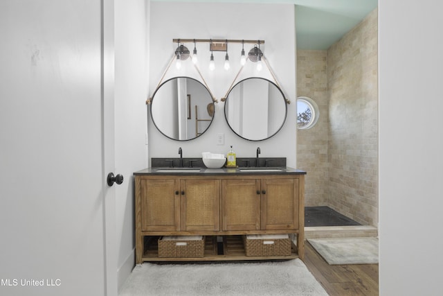 full bath with a sink, wood finished floors, double vanity, and a tile shower