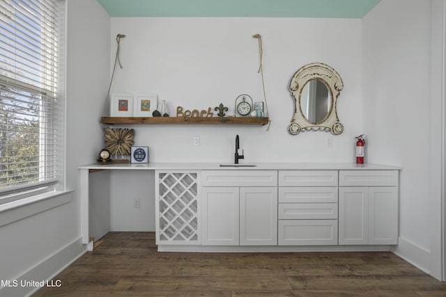 bar featuring indoor wet bar, baseboards, dark wood-style flooring, and a sink