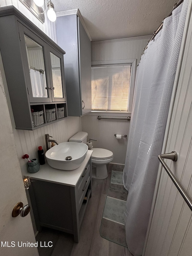 bathroom featuring toilet, a textured ceiling, ornamental molding, vanity, and hardwood / wood-style flooring