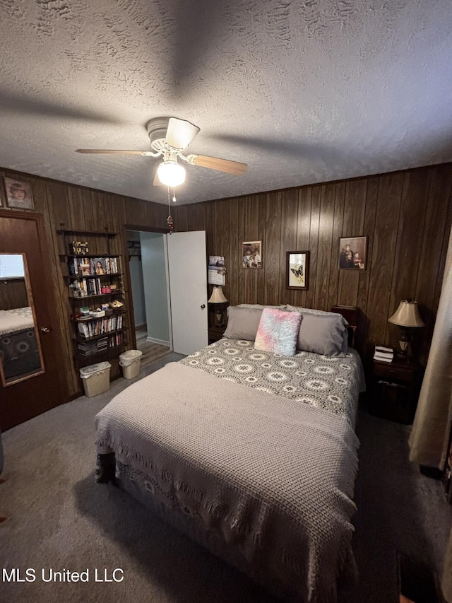 carpeted bedroom featuring ceiling fan, wooden walls, and a textured ceiling