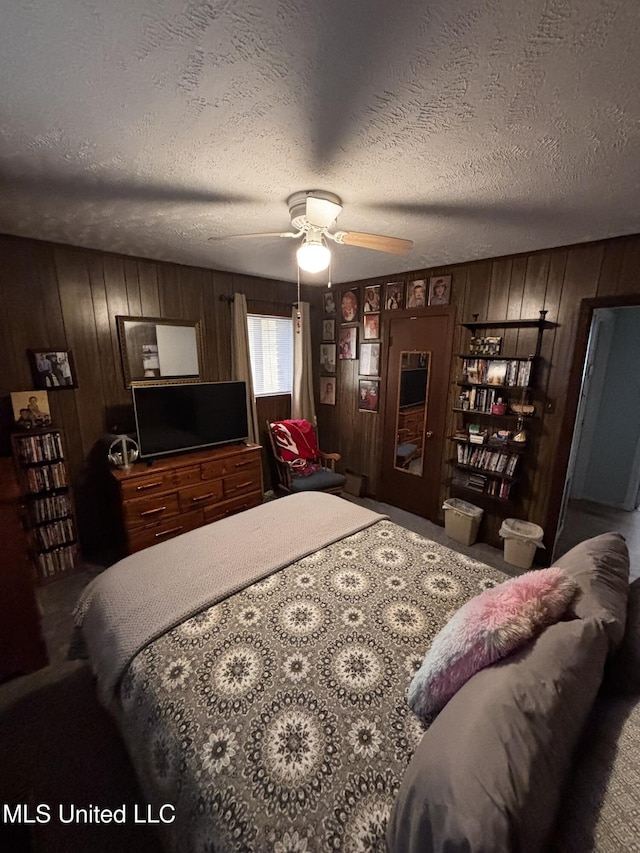 bedroom with ceiling fan, wooden walls, a textured ceiling, and carpet