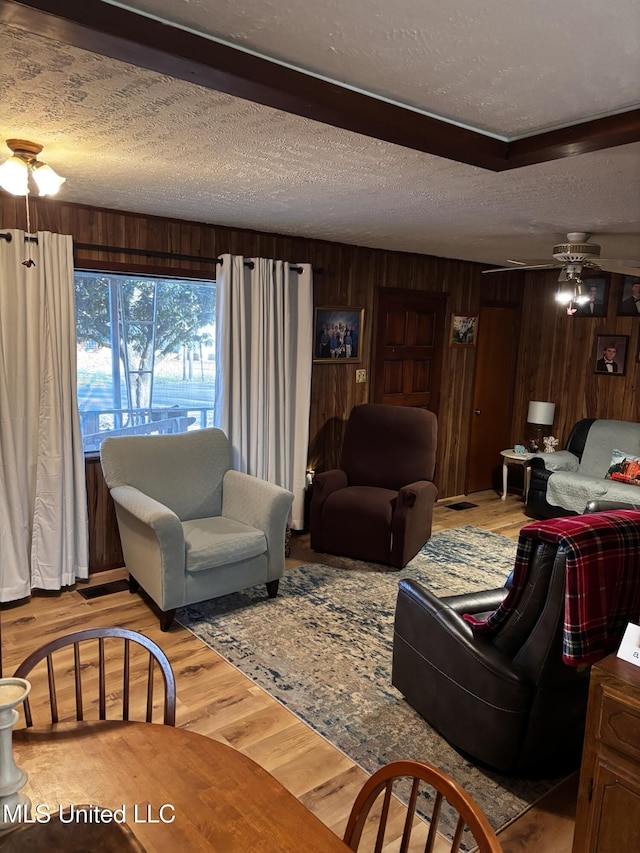 living room with ceiling fan, light hardwood / wood-style flooring, a textured ceiling, and wood walls