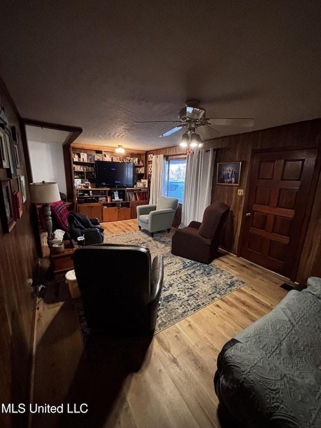 living room with hardwood / wood-style flooring, ceiling fan, a textured ceiling, and wood walls