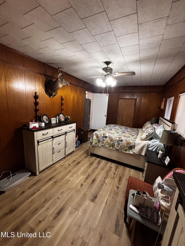 bedroom featuring light hardwood / wood-style flooring, wooden walls, and ceiling fan