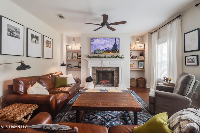 living area featuring a stone fireplace, visible vents, ceiling fan, and built in features