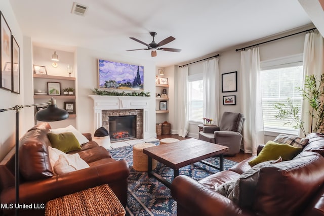 living room featuring ceiling fan, a stone fireplace, visible vents, baseboards, and wood finished floors