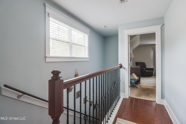 corridor with baseboards, visible vents, wood finished floors, and an upstairs landing