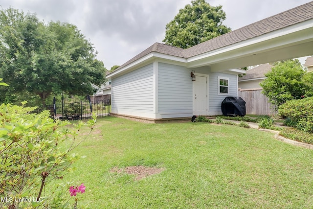 exterior space featuring fence, roof with shingles, and a lawn
