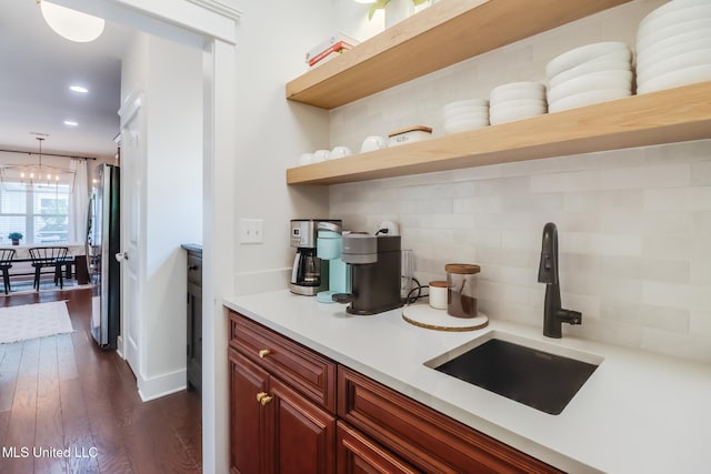 kitchen with freestanding refrigerator, decorative backsplash, light countertops, dark wood-style flooring, and a sink