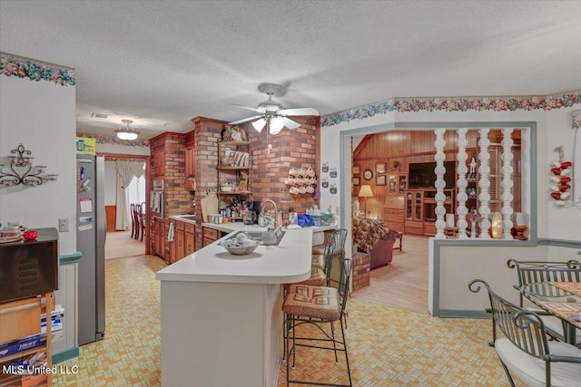 kitchen featuring sink, ceiling fan, a textured ceiling, kitchen peninsula, and a breakfast bar area