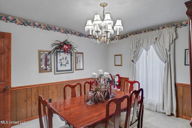 carpeted dining area featuring a chandelier, a textured ceiling, and wood walls