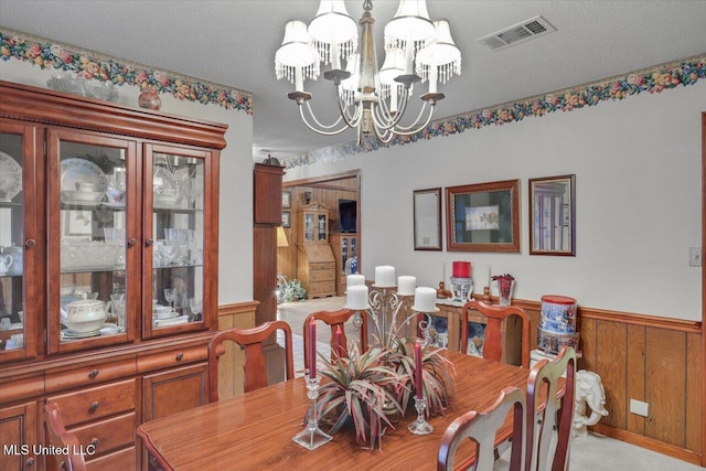 carpeted dining area featuring a textured ceiling, wooden walls, and a notable chandelier