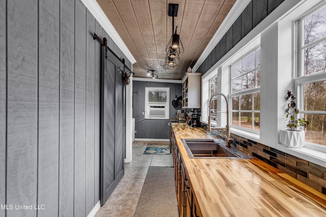 kitchen featuring a healthy amount of sunlight, butcher block countertops, a barn door, ornamental molding, and a sink