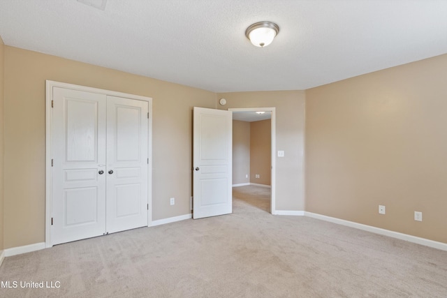 unfurnished bedroom featuring a textured ceiling, a closet, and light colored carpet