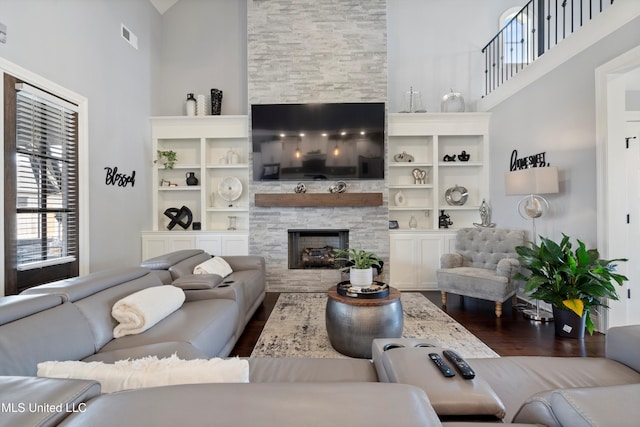 living room with a stone fireplace, built in shelves, high vaulted ceiling, and wood-type flooring