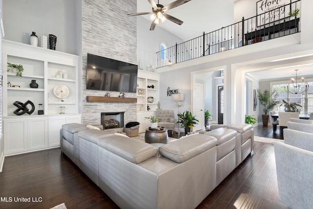 living room with built in shelves, high vaulted ceiling, dark hardwood / wood-style floors, a fireplace, and ceiling fan with notable chandelier