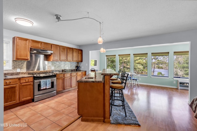 2529 Windward Dr, Gautier, MS 39553 - kitchen with gas range, a sink, under cabinet range hood, a breakfast bar area, and tasteful backsplash