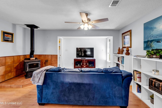 2529 Windward Dr, Gautier, MS 39553 - living area featuring a wood stove, a ceiling fan, wood finished floors, and a wainscoted wall
