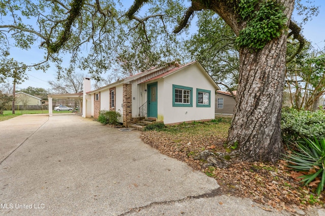 ranch-style home featuring concrete driveway, an attached carport, a chimney, and stucco siding