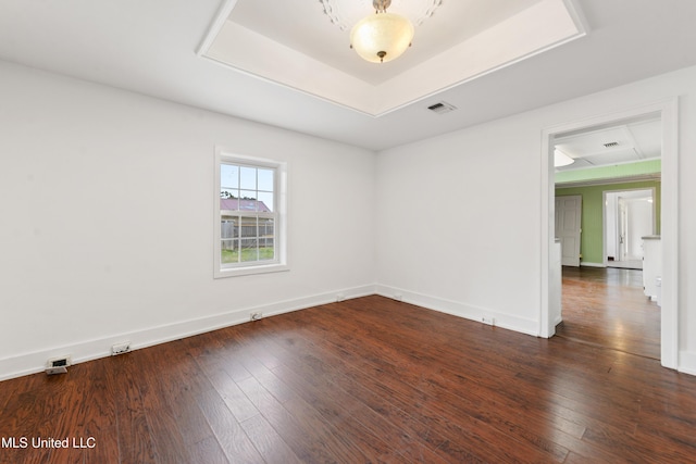 spare room with visible vents, a raised ceiling, dark wood finished floors, and baseboards