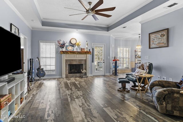 living room with a tiled fireplace, ornamental molding, and a raised ceiling