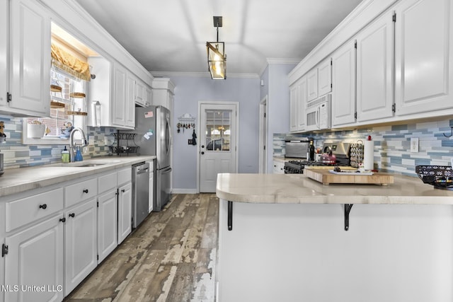 kitchen with sink, appliances with stainless steel finishes, hanging light fixtures, ornamental molding, and white cabinets