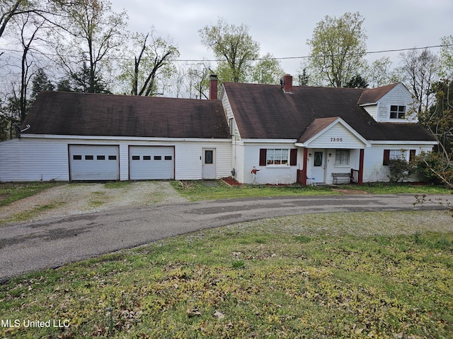 cape cod house with driveway, a chimney, an attached garage, and a front yard