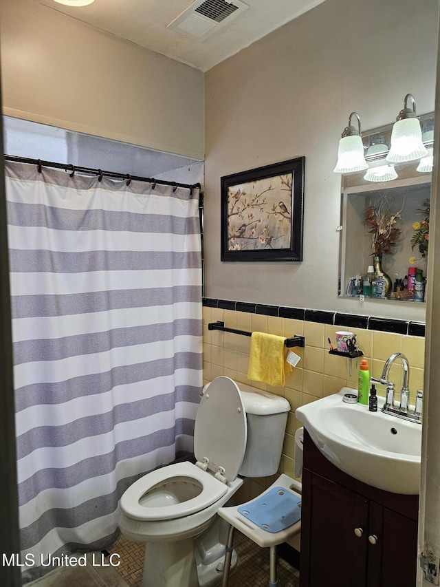 full bathroom with vanity, tile walls, toilet, a wainscoted wall, and visible vents