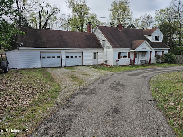 cape cod-style house with driveway, a garage, and a chimney