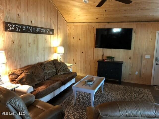 living room featuring hardwood / wood-style floors, wood walls, ceiling fan, and wooden ceiling