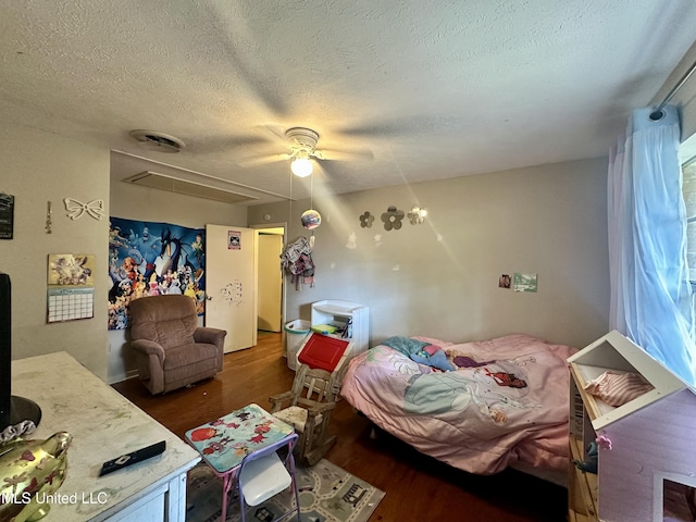 bedroom featuring a textured ceiling, a ceiling fan, attic access, and wood finished floors