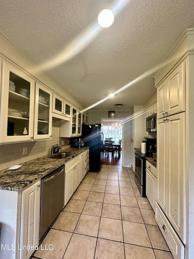 kitchen with a sink, a textured ceiling, stainless steel appliances, light tile patterned floors, and glass insert cabinets